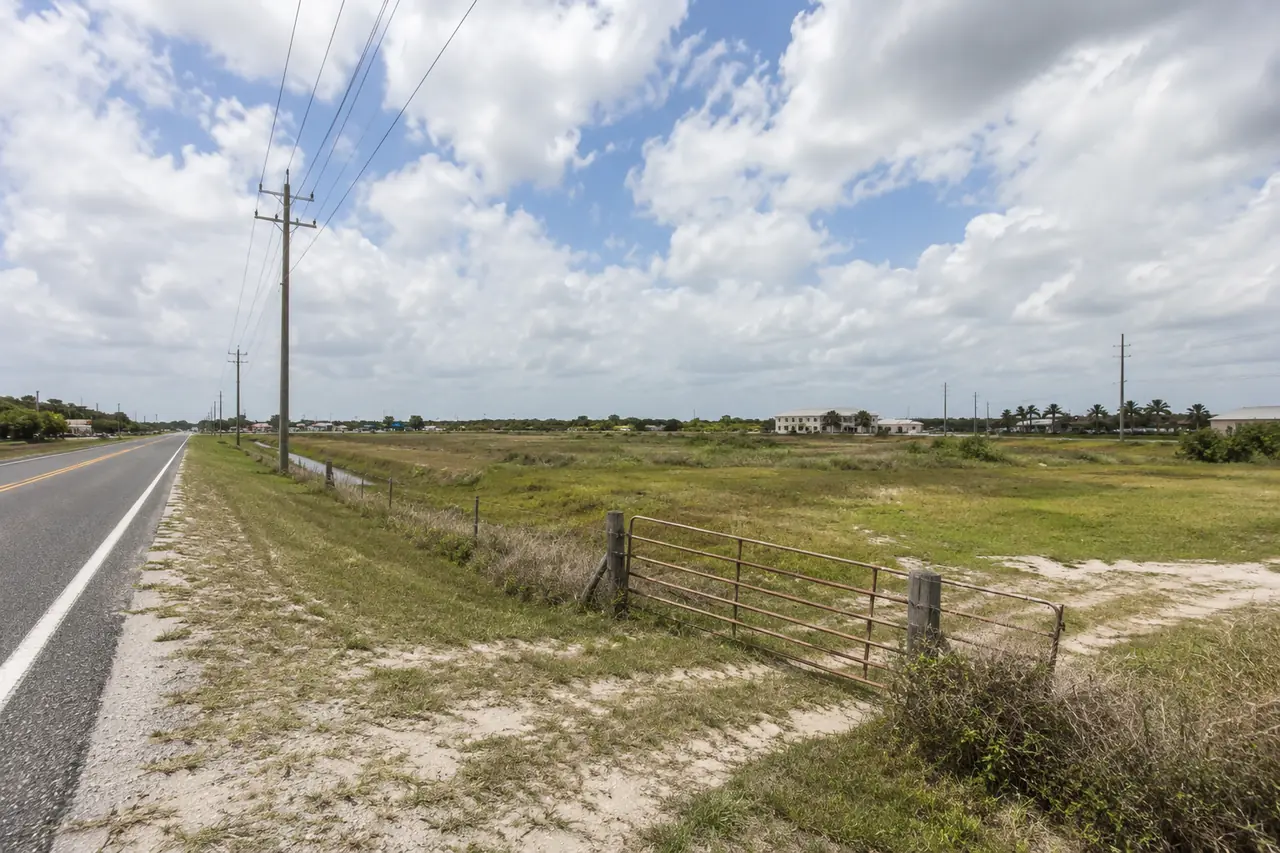 Undeveloped commercial land along a Florida highway with utility lines and an access gate